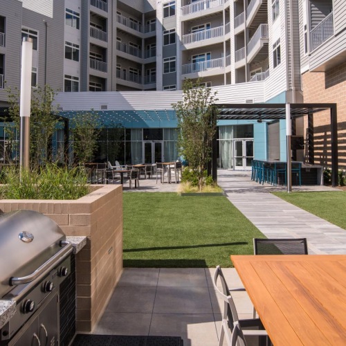 a patio with a grill and a table and a building with a pool
