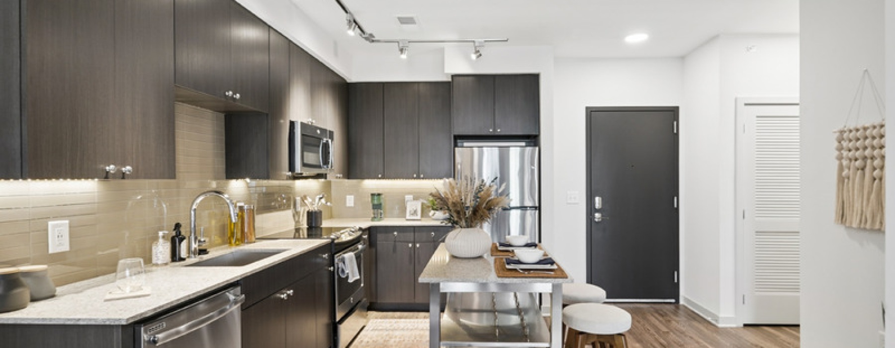 Apartment kitchen at The Daley at Shady Grove featuring stainless steel appliances, quartz countertops, large island, and modern cabinetry in Rockville, Maryland
